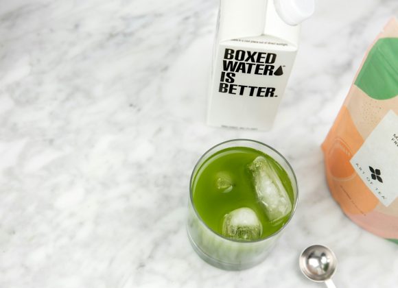 a glass of green liquid next to a bottle of water